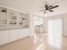 Built-in shelving with lower cabinetry, ceiling fan, tile flooring, and sliding glass door with vertical blinds