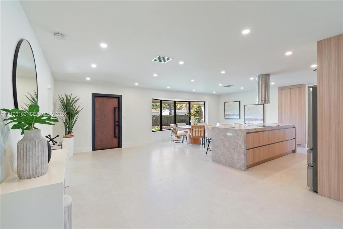 Open-concept space featuring large-format tile flooring, recessed ceiling lighting, a waterfall-edge kitchen island, natural wood-finish cabinetry, an