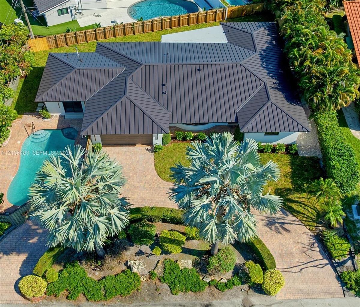 Aerial perspective of a residence featuring a dark metal roof, paver driveway, private swimming pool, and mature landscaping