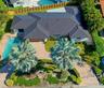 Aerial perspective of a residence featuring a dark metal roof, paver driveway, private swimming pool, and mature landscaping