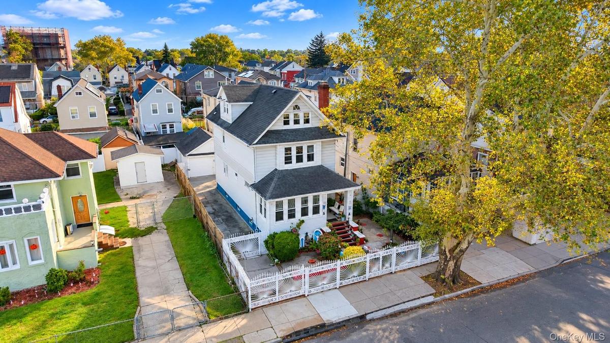Three-story residence featuring a covered front porch, white siding, a paved driveway, and a fenced front yard with mature landscaping