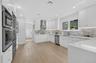 Kitchen featuring white cabinetry, quartz countertops, tile backsplash, stainless steel appliances, and wood-finish flooring