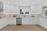 Kitchen featuring white shaker-style cabinetry, a mosaic tile backsplash, stainless steel dishwasher, light-toned wood-finish flooring, and under-cabi