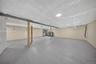 Unfinished lower-level space featuring spray foam wall insulation, vapor-barrier ceiling insulation, painted concrete flooring, structural support pil