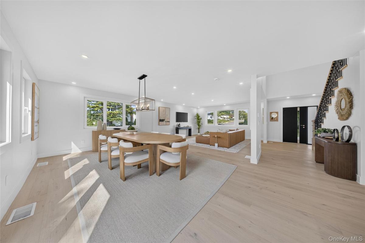 Open-concept living space featuring wood-finish flooring, recessed lighting, a geometric metal-frame chandelier, and a staircase with a black iron rai