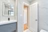 Floating vanity with a textured grey facade, integrated rectangular sink, wall-mounted matte black faucet, illuminated vanity mirror, and large-format