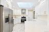Kitchen featuring white shaker-style cabinetry, stainless steel appliances, quartz countertops, a large skylight, and stone-finish tile flooring