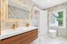 Floating dual-sink vanity with wood-finish cabinetry, quartz countertop, gold-tone fixtures, backlit rectangular mirror, and floor-to-ceiling stone-pa