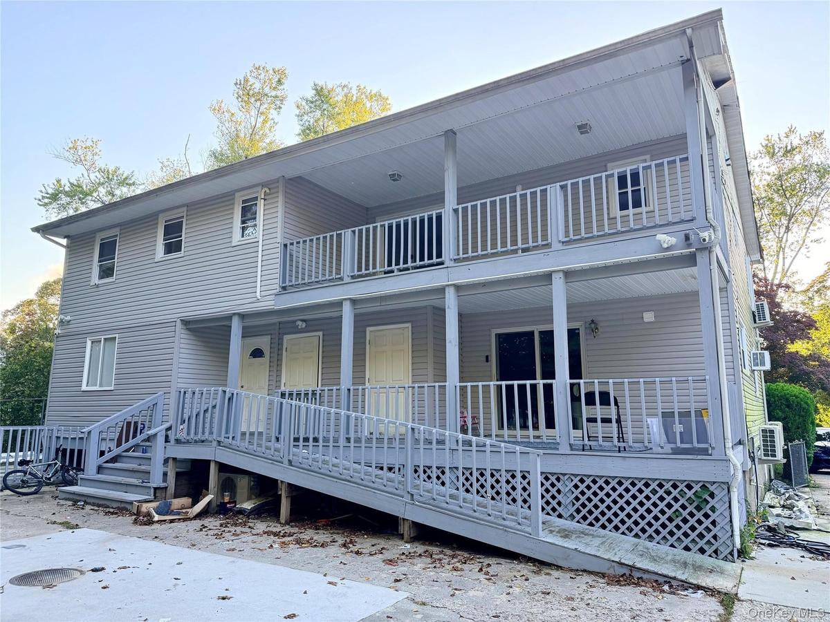 Two-story exterior featuring light gray vinyl siding, a full-length covered porch, a second-level balcony with railings, and an integrated wood-frame 