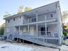 Two-story exterior featuring light gray vinyl siding, a full-length covered porch, a second-level balcony with railings, and an integrated wood-frame 