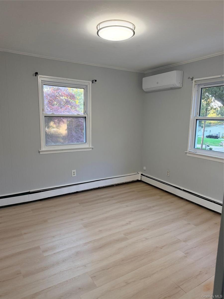 Neutral-toned interior featuring wood-finish flooring, a wall-mounted ductless mini-split system, dual windows, and a flush-mount circular ceiling lig