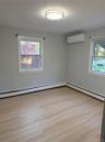 Neutral-toned interior featuring wood-finish flooring, a wall-mounted ductless mini-split system, dual windows, and a flush-mount circular ceiling lig