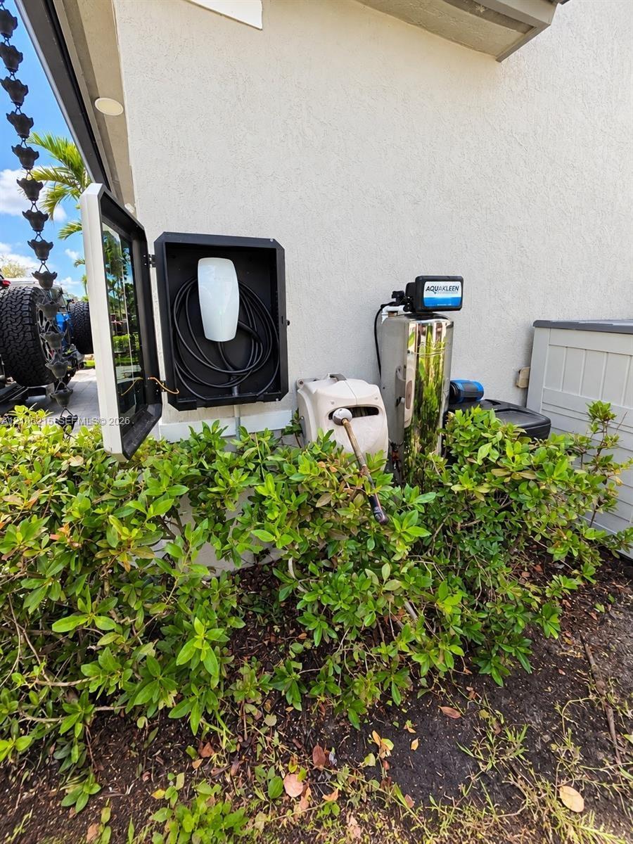 Exterior charging station featuring a wall-mounted electric vehicle charger enclosed in a protective housing, accompanied by a whole-home water filtra
