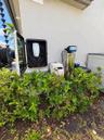 Exterior charging station featuring a wall-mounted electric vehicle charger enclosed in a protective housing, accompanied by a whole-home water filtra