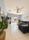 Living area featuring vaulted ceilings, light-tone tile flooring, a mounted ceiling fan, and sliding glass doors with roller shades