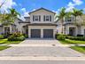 Two-story residence featuring a tile roof, neutral stucco exterior, stacked stone accents, and a paved two-car garage driveway