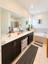 Bathroom featuring a dual-sink vanity with dark cabinetry, stone-finish countertops, full-width mirror, tile flooring, and a deep soaking tub
