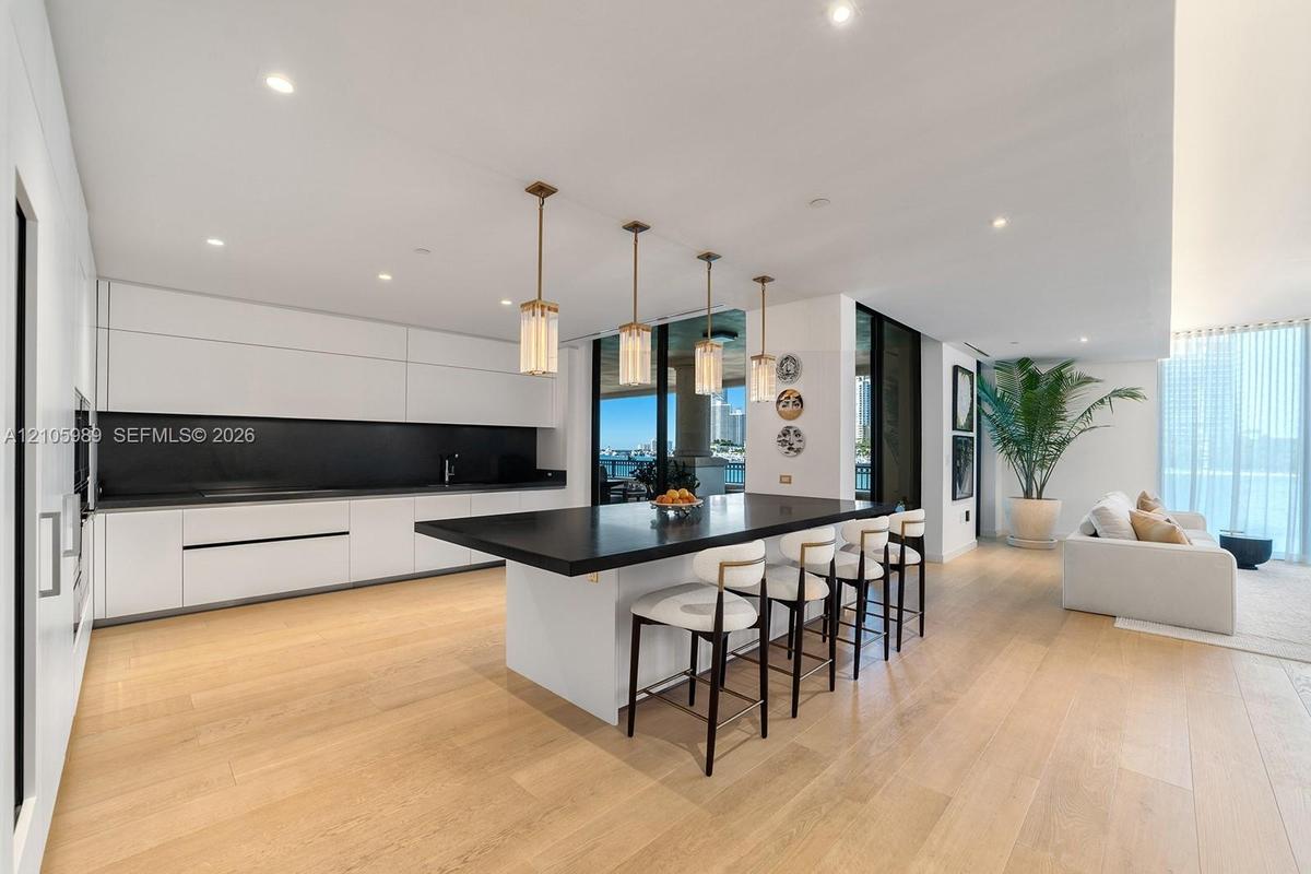 Modern kitchen featuring flat-panel cabinetry, a central island with a solid surface countertop, wood-finish flooring, recessed lighting, and four cyl