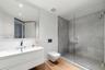 Floating white vanity with a rectangular sink, wall-mounted toilet, walk-in shower with a glass enclosure and stone-tile surround, and wood-finish flo