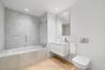 Bathroom featuring a white floating vanity, wall-mounted toilet with a chrome flush plate, glass-enclosed shower over tub combination, large frameless