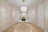 Foyer featuring light-toned wood-finish flooring, textured wall coverings, a tiered crystal chandelier, full-height flush doors with metallic casing, 