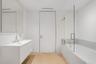 Wall-mounted floating vanity with integrated rectangular sink, wood-finish chevron flooring, frameless glass shower enclosure, and stone-surround soak