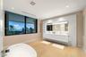 Floating dual vanity with integrated countertop, floor-to-ceiling stone wall treatment, back-lit mirror, freestanding soaking tub, and large-format bl