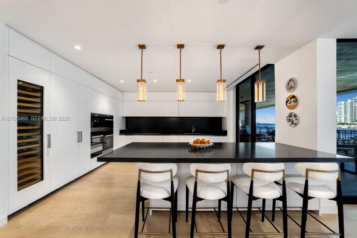 Sleek kitchen featuring flat-panel cabinetry, a spacious center island with a dark countertop, integrated wine refrigeration, built-in wall ovens, and