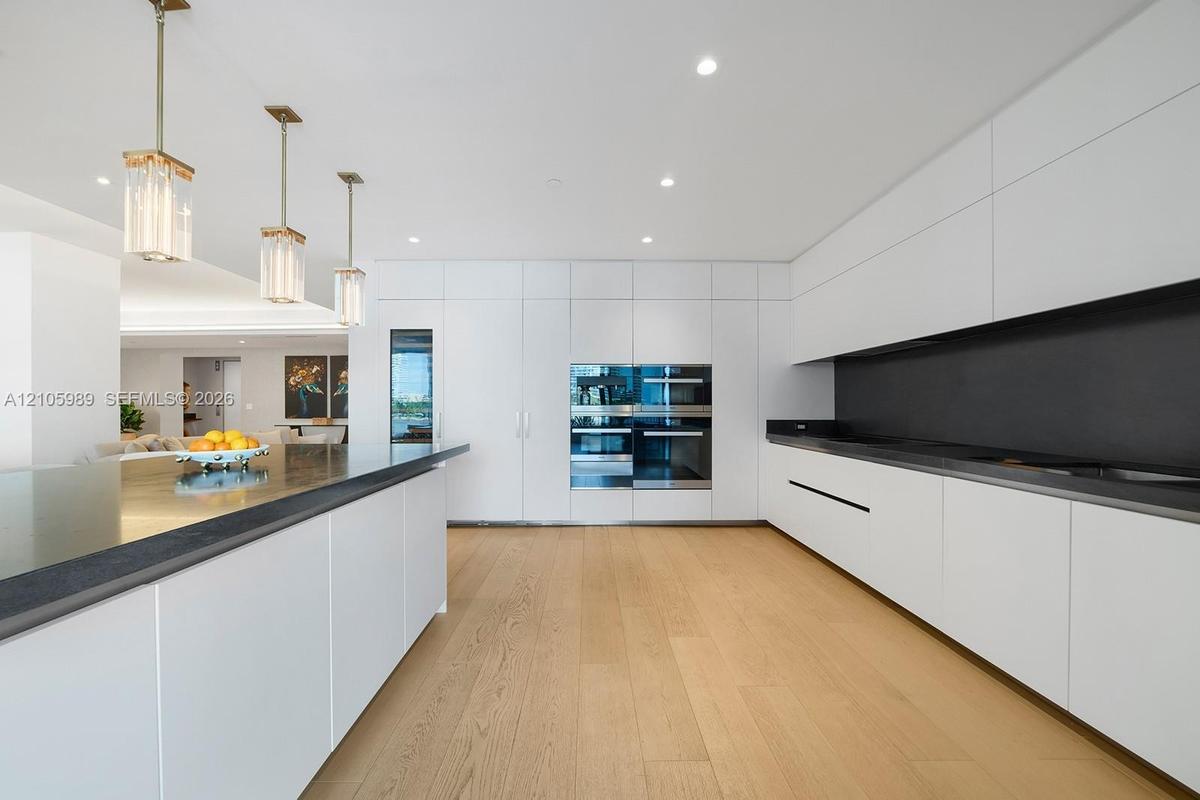 Kitchen featuring flat-panel cabinetry, a spacious island with a dark countertop, integrated double wall ovens, wood-finish flooring, and pendant ligh