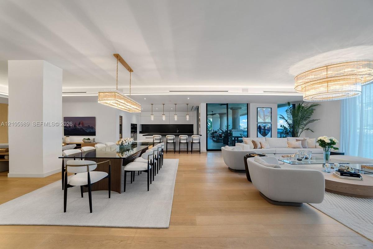 Open-concept interior featuring wood-finish flooring, linear pendant lighting, tiered crystal chandelier, recessed cove lighting, and floor-to-ceiling