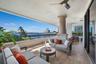 Covered balcony featuring wood-finish flooring, a textured stone column, black metal railing, and a mounted ceiling fan