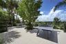 Expansive outdoor terrace featuring large-format tile flooring, perimeter glass railing, mature landscaping, and integrated landscape lighting