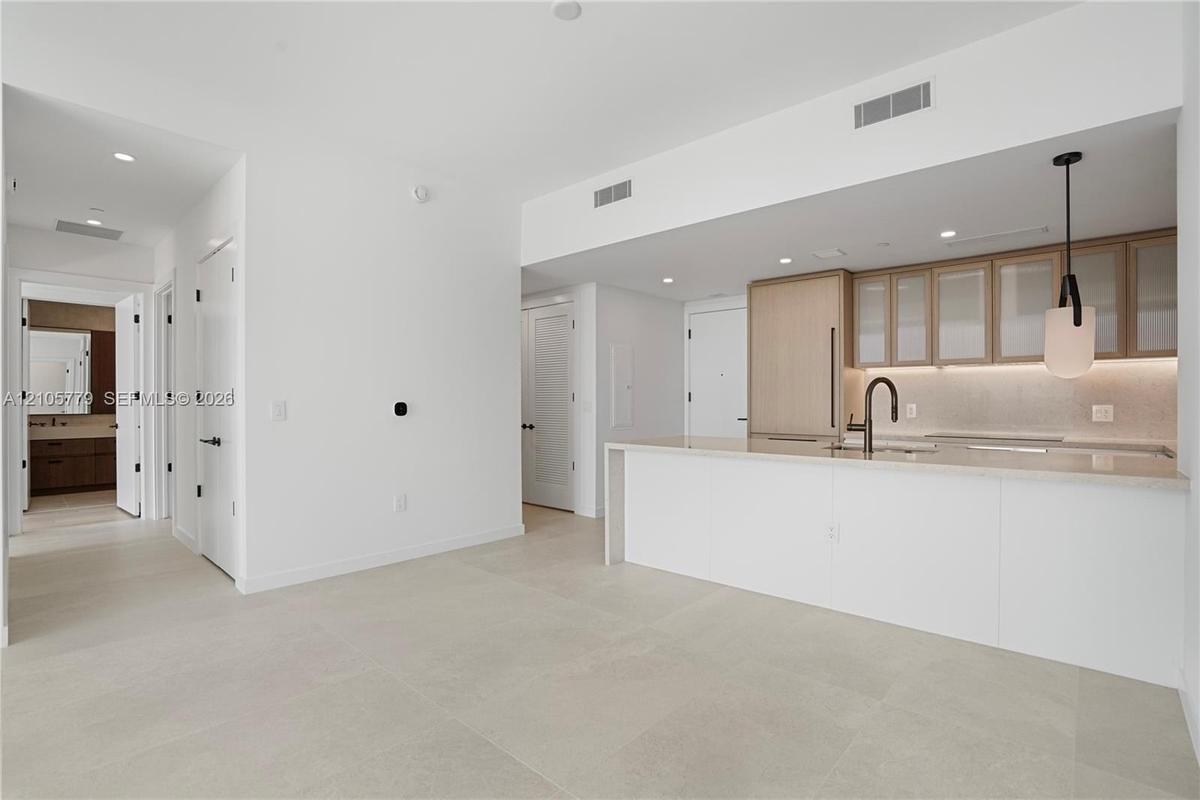 Kitchen featuring a stone-surface island, light-finish cabinetry, under-cabinet lighting, a matte black faucet, and large-format tile flooring