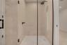 Walk-in shower featuring floor-to-ceiling neutral tile, glass enclosure with matte black hardware, rainfall showerhead, and wall-mounted matte black f