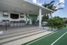 Covered outdoor kitchen featuring built-in stainless steel appliances, a stone-surfaced bar, tile flooring, and a decorative wall mural, situated besi