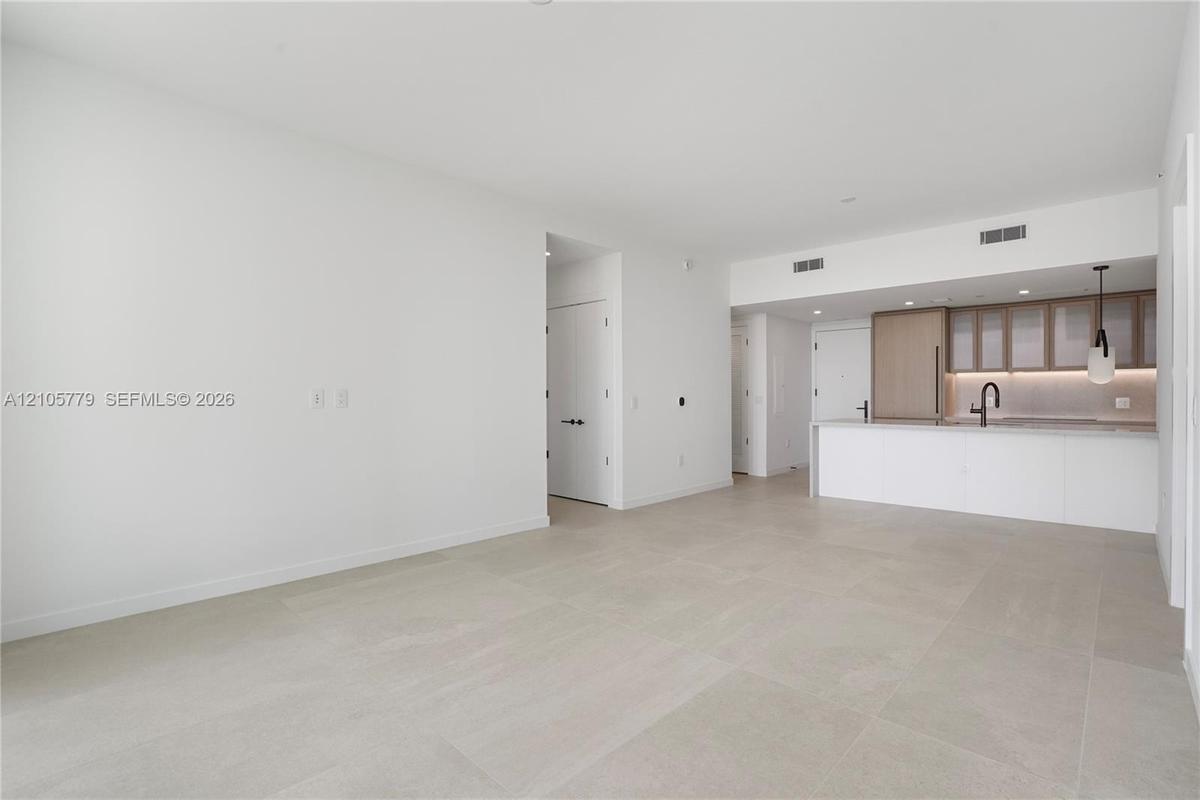Open-concept interior featuring large-format tile flooring, kitchen with light wood cabinetry, integrated appliances, stone-surface counters, and matt