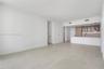 Open-concept interior featuring large-format tile flooring, kitchen with light wood cabinetry, integrated appliances, stone-surface counters, and matt