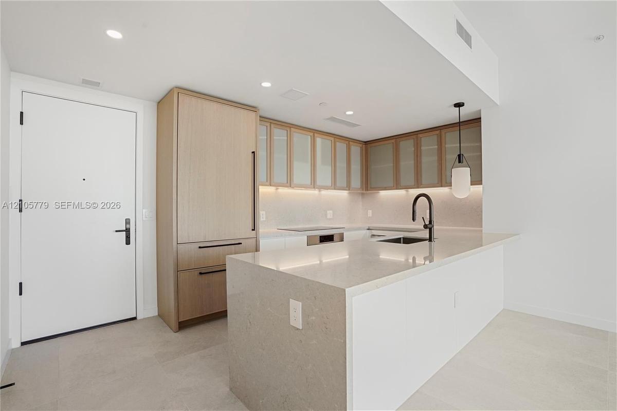 Kitchen featuring an oversized stone-surfaced island, flat-panel wood cabinetry, paneled-front refrigerator, under-cabinet lighting, and a matte black