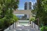 Stone staircase featuring metal handrails, framed by mature landscaping, leading to a plaza with a prominent masonry structure and glass railing