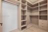 Walk-in closet featuring custom built-in shelving, integrated hanging rods, three soft-close storage drawers, and light-tone wood-finish flooring