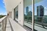 Expansive covered balcony featuring glass panel railings, floor-to-ceiling sliding glass doors, and neutral concrete-style flooring