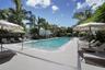 Rectangular swimming pool featuring a light-toned paved deck, metal handrails, and surrounding mature palm trees