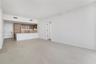 Open-concept interior with large-format neutral tile flooring, minimalist kitchen featuring light wood-tone cabinetry, stone-surface breakfast bar, an