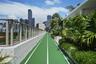 Outdoor running track featuring a high-traction surface, glass panel perimeter railing, and built-in landscape planters containing mature palm trees a