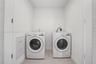Laundry space featuring white front-loading appliances, neutral tile flooring, and louvered privacy doors