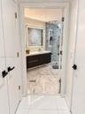 Floating vanity with solid-surface countertop, LED-backlit mirror, glass-enclosed shower with tiled surround, and large-format stone-finish flooring