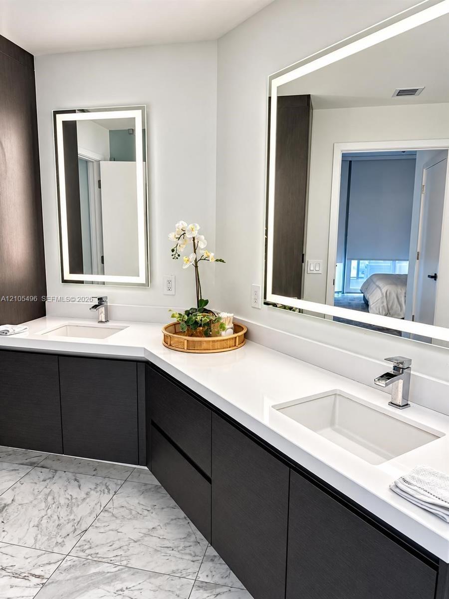 Dual-vanity bathroom featuring dark wood-finish cabinetry, white stone-composite countertops, integrated rectangular sinks with polished chrome faucet