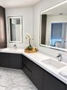 Dual-vanity bathroom featuring dark wood-finish cabinetry, white stone-composite countertops, integrated rectangular sinks with polished chrome faucet