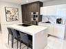 Kitchen featuring a waterfall-edge island with an integrated cooktop, flat-panel cabinetry, a stone-pattern backsplash, and stainless steel built-in a