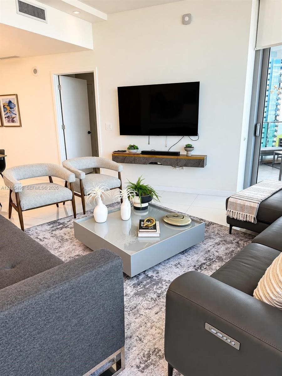 Living area featuring large-format tile flooring, recessed ceiling lighting, and a wall-mounted floating media console
